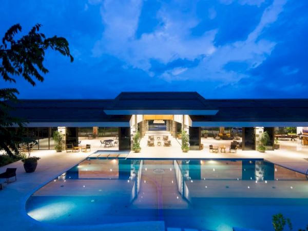 The image shows a luxurious modern building with a glowing pool in the foreground, set against a dramatic evening sky.