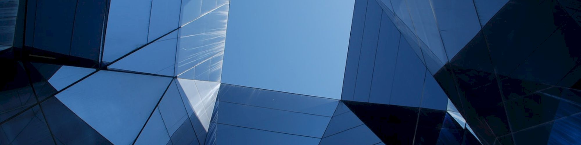 Blue geometric glass structures form a pattern, creating an abstract architectural view with a central open sky area.