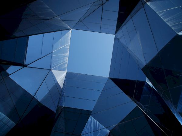 Abstract view of a geometric glass structure with a blue sky visible through the center, creating a symmetrical and modern architectural effect.