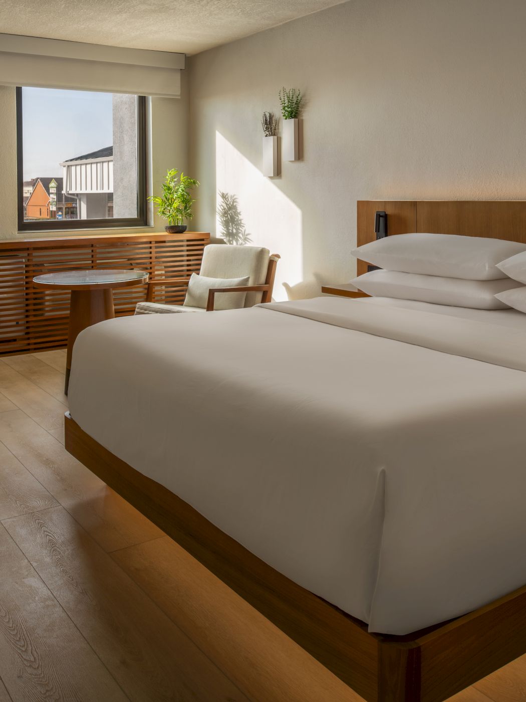 A modern hotel room with a large bed, wooden furniture, a seating area by the window, and warm ambient lighting ending this sentence.