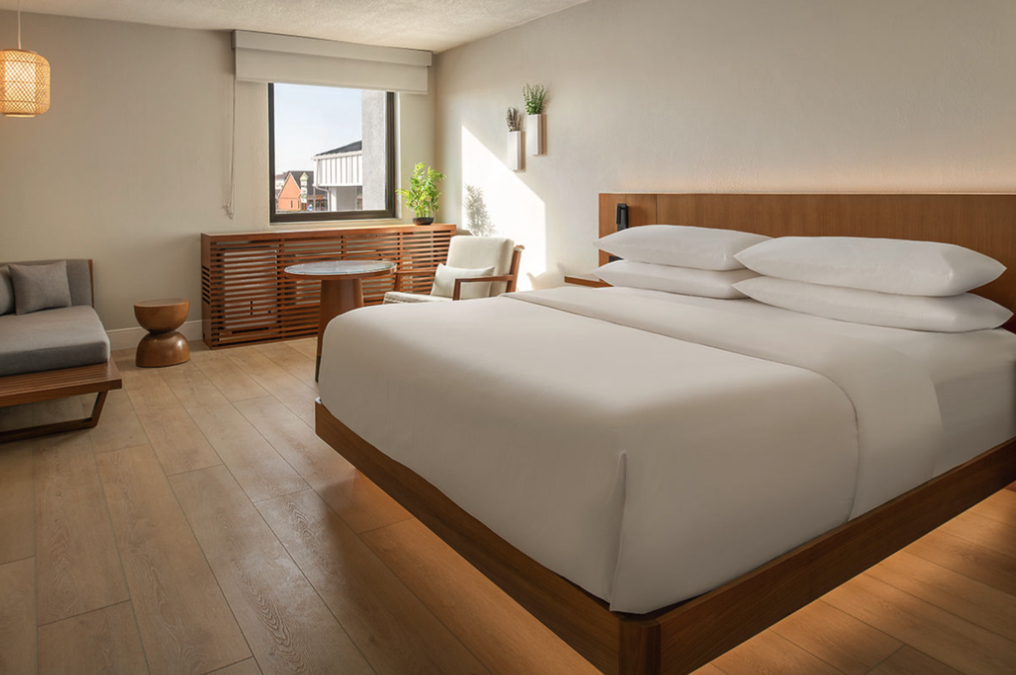A modern hotel room with a large bed, wooden furniture, soft lighting, and a small seating area by the window. Ends in a period.