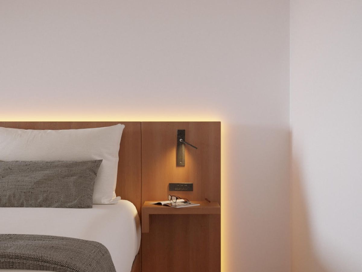 A modern bedroom corner with a bed, wooden nightstand, wall lamp, and minimal decor, exuding a warm and cozy ambiance.