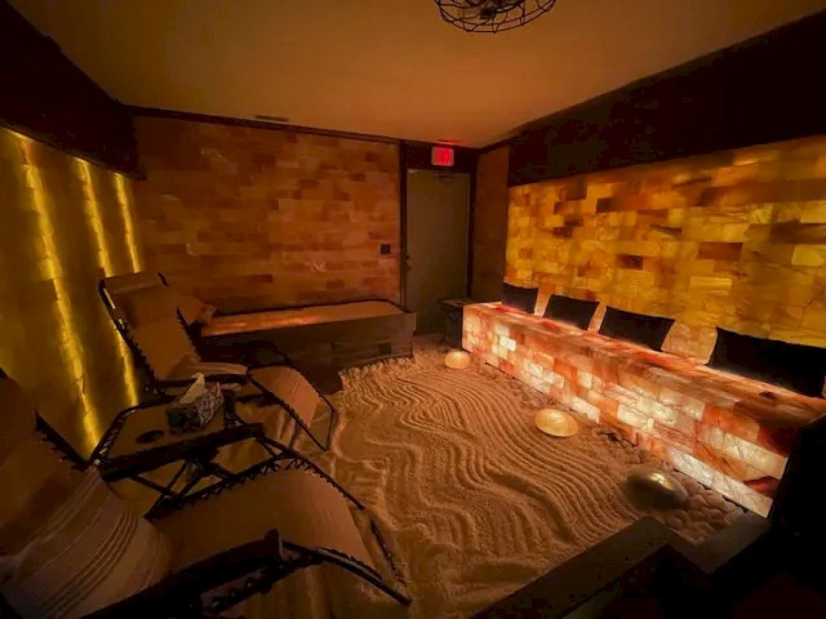 A dimly lit room with salt block walls, lounge chairs, and a sandy floor, creating a cozy and tranquil atmosphere.