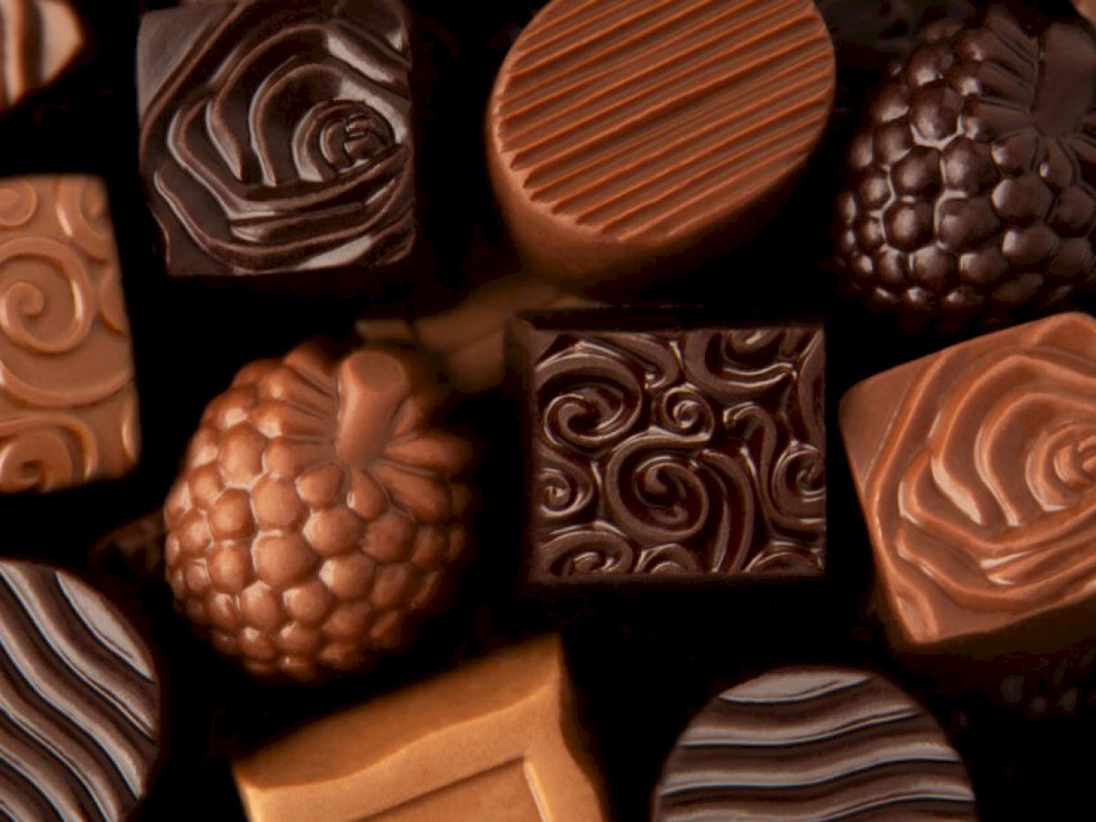 The image shows an assortment of intricately designed chocolates, featuring various patterns in shades of brown and dark brown.