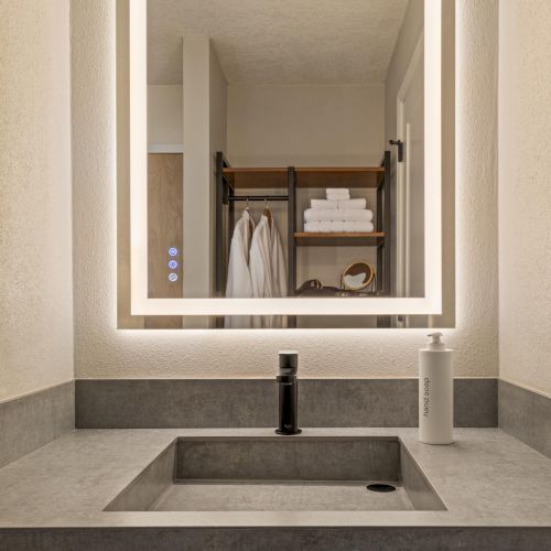 Bathroom vanity at The Amaya with an illuminated mirror, modern stone sink, and clean, minimalist finishes