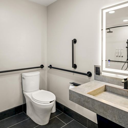 Accessible bathroom at The Amaya featuring grab bars, an illuminated mirror, and a clean, modern layout