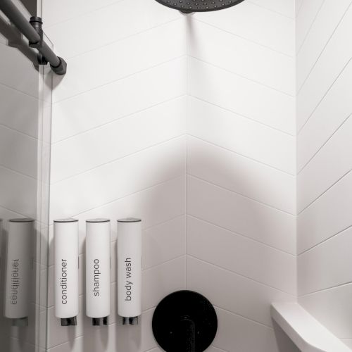 Walk-in shower at The Amaya with a rain shower head, black fixtures, and minimalist tilework