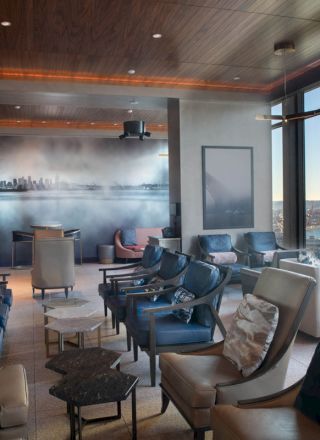 This image shows a stylish lounge with seating, large windows, and a view of the water and hills outside.