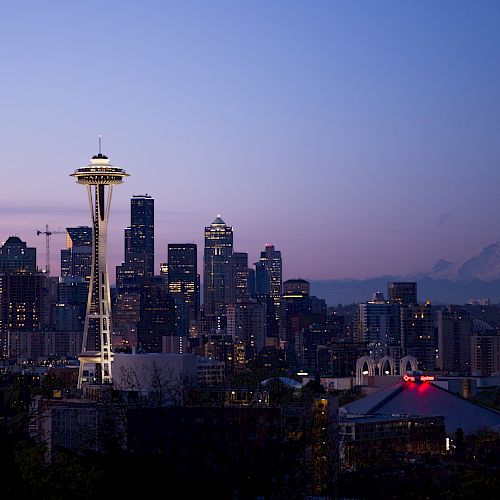 The image shows a city skyline at dusk, featuring a prominent tower and buildings with a mountain in the background.