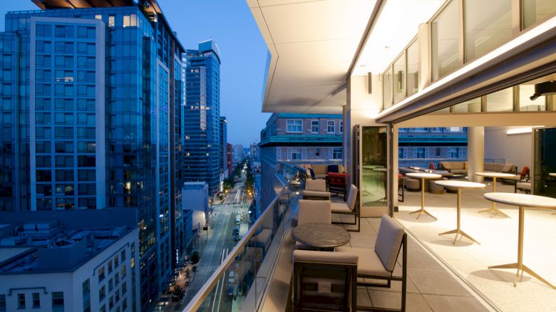 A modern rooftop terrace with seating overlooks a cityscape with tall buildings during the evening.